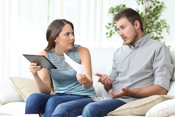 Angry wife with tablet showing receipt to husband at home