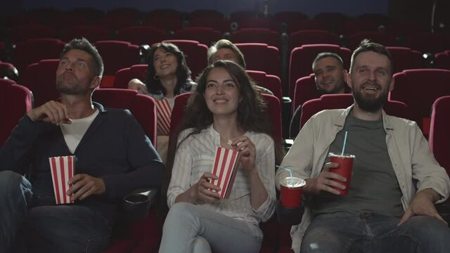 Medium shot of several diverse people sitting in cinema, watching funny movie and laughing