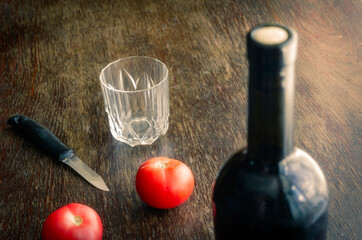 Full bottle of wine with cork, two red tomatoes,  knife and an empty glass.