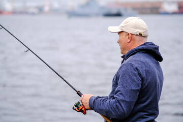 A fisherman in a baseball cap with a fishing rod in his hands smiles. Concept of healthy outdoor recreation.