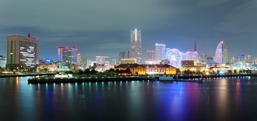 Fototapeta premium Beautiful night scenery of Yokohama Minatomirai Bay area with high rise buildings in the background, a giant Ferris wheel in Cosmo World Amusement Park & colorful reflections of city lights on water