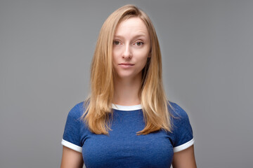 Portrait of young beautiful woman with blond hair and in blue T shirt look at camera, posing in studio, isolated on grey studio background