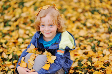 baby - little boy with curly blond hair smiling against the background of yellow autumn leaves in the Park