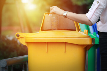 Someone or a woman dump a plastic bottle garbage to yellow recycle bin in a park