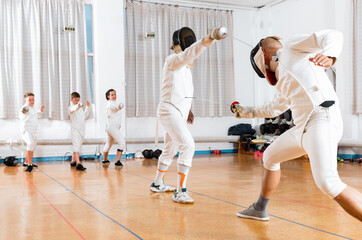 Positive smiling coaches demonstrating to young athletes attack movements with rapier during...