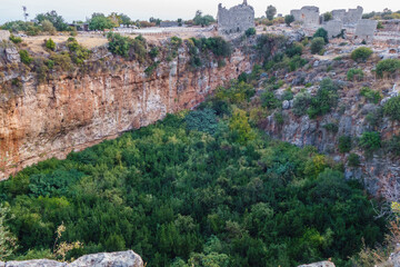 Panoramic view onto ruins of buildings in ancient city Kanli Divane or Canytelis, Ayaş, Turkey. All main buildings standing near huge karst sinkhole (maximum diameter about 130 m, depth about 70 m)