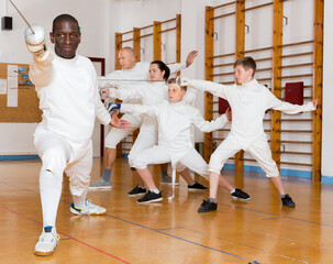 African American man wearing fencing uniform practicing with foil at gym