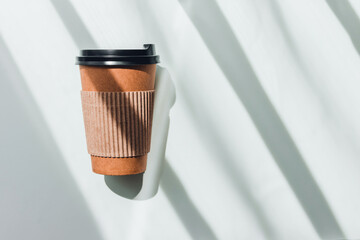 Craft paper coffee cup with hard shadows on white table.