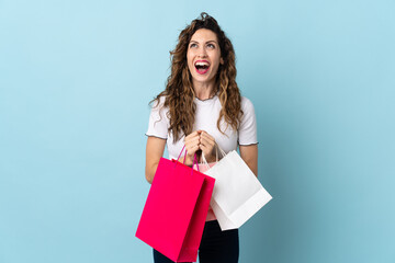 Fototapeta na wymiar Young caucasian woman isolated on blue background holding shopping bags and surprised