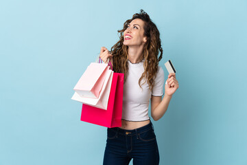 Young caucasian woman isolated on blue background holding shopping bags and a credit card