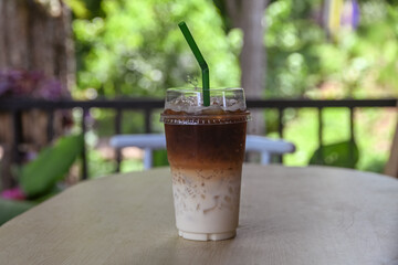 iced coffee in plastic cup for take away on wooden bar with green nature in garden