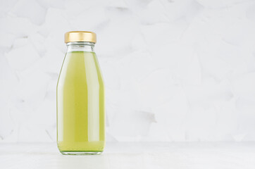 Green kiwi juice in glass bottle with gold cap mock up on white wood table in light interior with copy space, template for packaging, advertising, design product, branding.