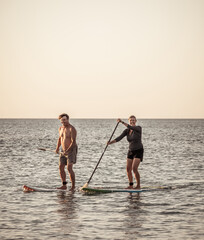 Mature couple on SUP, stand up paddle board, having fun on quiet sea at sunset
