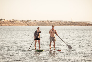 Mature couple on SUP, stand up paddle board, having fun on quiet sea at sunset