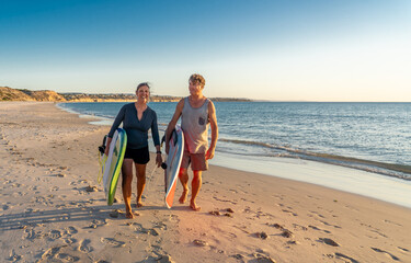 Mature couple surfers with surfboard having fun on empty remote beach enjoying outdoors lifestyle