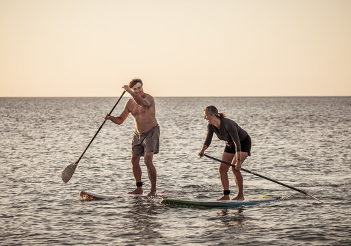 Mature Couple On SUP, Stand Up Paddle Board, Having Fun On Quiet Sea At Sunset