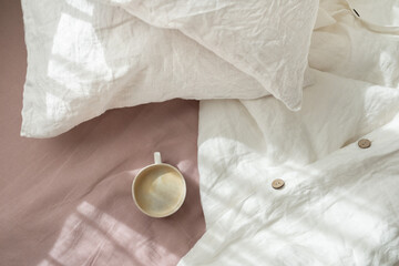 Cup of fresh coffee in bed, morning mood. Linen cotton textile bedclothes. Organic and natural linen. Cozy bedroom interior. Beautiful light.