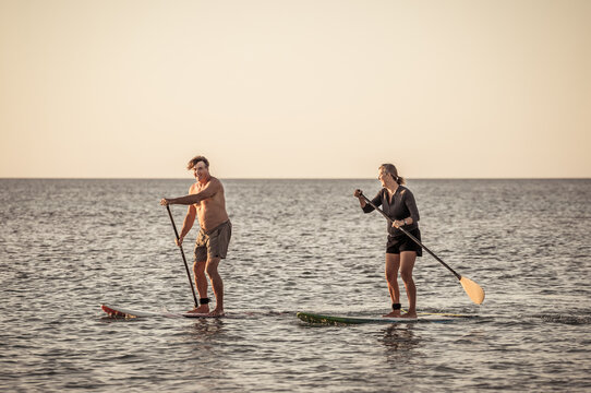 Mature Couple On SUP, Stand Up Paddle Board, Having Fun On Quiet Sea At Sunset