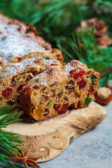 Traditional Christmas fruit cake on a wooden board in festive decoration, dark background.