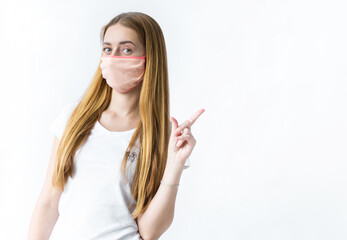 A young girl in a mask from a virus shows her index finger to the side on a white background. Coronavirus and security theme