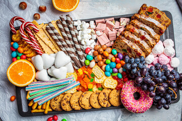 Christmas sweets platter. Christmas fruit cake, candy, chocolate, candy cane, cookies, fruit on black tray.