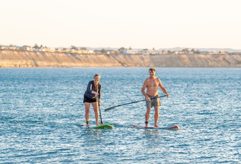 Mature couple on SUP, stand up paddle board, having fun on quiet sea at sunset