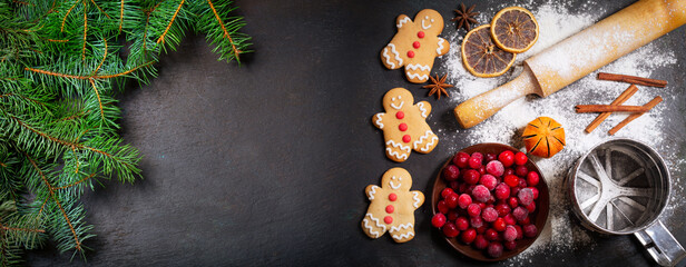 Christmas background. Fresh fir branches and gingerbread cookies with ingredients for christmas baking on dark background