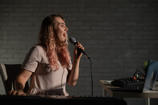A young European woman sings into a microphone and accompanies on an electronic piano. The girl shoots a video blog. Remote vocal lesson. A female singing teacher conducts online classes.
