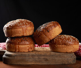 baked round crispy sesame buns for burgers on brown wooden board