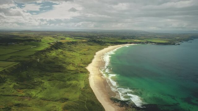White Beach sand coast aerial zooming, Antrim County, Nortern Ireland. Epic landscape of greenness cliff shore of Atlantic ocean bay. Calm water at dusk cloudy day. Footage shooting shot in 4K, UHD