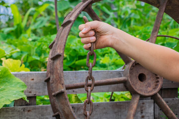Hand holds a chain of iron and a hammer near a large iron wheel
