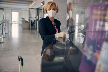 Blonde woman in medical mask standing at check-in desk in airport