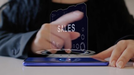 Female hand interacts HUD hologram with text Sales. Woman in black uses conceptual holographic technology of the future on the screen of a smartphone lying on a table