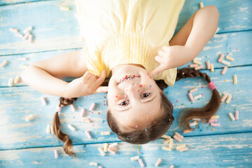 Funny emotional little girl with sprinkled lips and freckles on color background with colorful candies