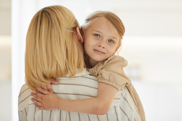 Warm-toned close up portrait of cute little girl embracing happy mother with love while sitting in her arms looking at camera and smiling, copy space