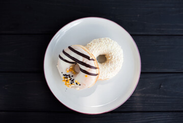 Top-view of two assorted donuts on a small white plate with black background. Fresh sweet colorful homemade vanilla donuts on vintage background for birthday or party, free space for text