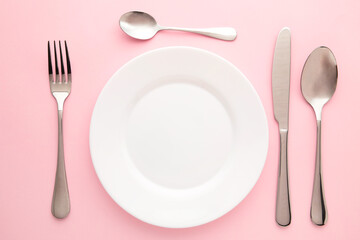 Table setting with white plates, and cutlery - fork, spoon and knife. Shot from above. Copy space on empty plate.