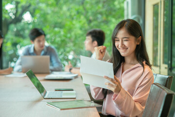 Asian girl reading good news in a letter in a desktop at office.