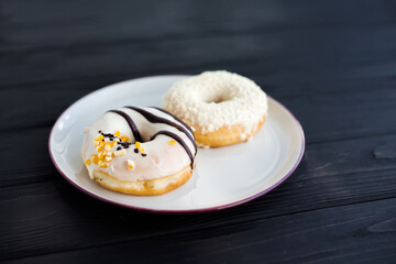 Close-up of two assorted donuts on a small white plate with black background. Fresh sweet colorful homemade vanilla donuts on vintage background for birthday or party, free space for text