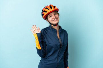 Young cyclist woman isolated on blue background saluting with hand with happy expression - obrazy, fototapety, plakaty