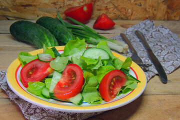 salad with cucumber, tomato and onion. Salad with greens, cherry tomatoes, red onions and cucumber on white plate with wood background, overhead view with fork