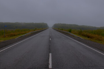 Straight track in fog. Kilometer post. Two-lane road. Early morning, thick fog