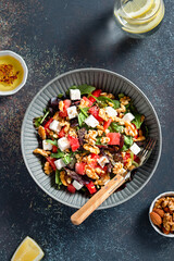 Summer refreshing salad with watermelon, feta cheese, walnuts and greens on black table top with lemon water, vertical image, top view. Recipe for heat wave