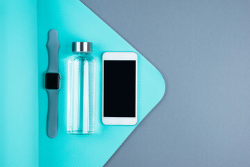 Top view of reusable eco glass water bottle, smart mobile phone and tracker watch on turquoise blue...