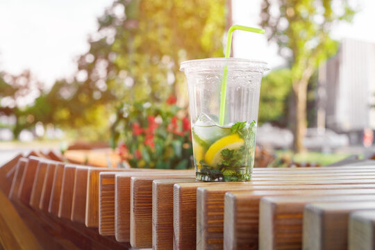 Mojito in a plastic glass on a wooden bench. Cold citrus cocktail close up.