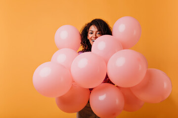 Fototapeta na wymiar Attractive pleasant woman holding helium balloons on yellow background. Studio shot of chilling birthday girl smiling to camera.