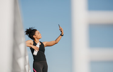 Selfie for sports blog. Smiling african american girl with bottle makes photo at smartphone