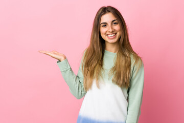 Young woman over isolated pink background holding copyspace imaginary on the palm to insert an ad