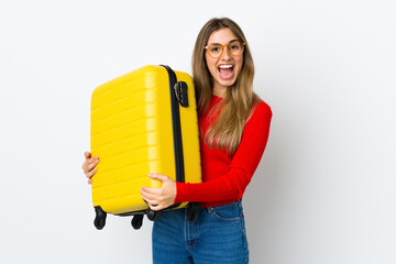 Young woman over isolated white background in vacation with travel suitcase and surprised