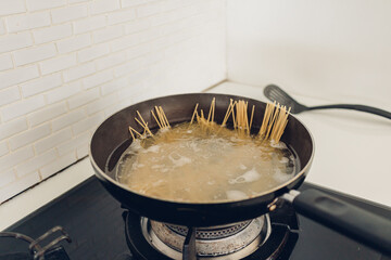 Image of boiling spaghetti with the pan in white kitchen.